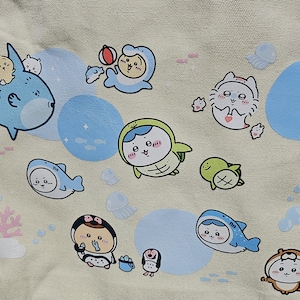 May include: A beige fabric featuring a repeating pattern of cartoon sea creatures, including sharks, dolphins, penguins, and turtles. The illustrations are in shades of blue, green, and white, with light blue circles and pink coral accents.