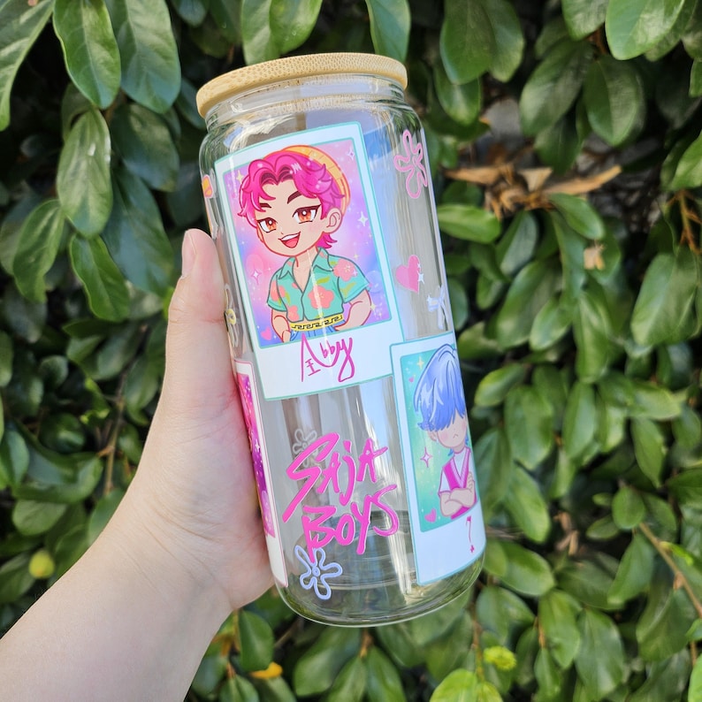 May include: A clear glass can-shaped tumbler with a bamboo lid. The tumbler features cartoon illustrations and the text "Spit Boys" in pink. The illustrations include a character with pink hair and another with blue hair.
