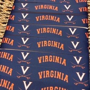 May include: A navy blue grosgrain ribbon featuring a repeating pattern of the orange text VIRGINIA and a white V logo with crossed sabers. The ribbon has a textured, ribbed surface and is arranged in multiple horizontal rows across the frame.
