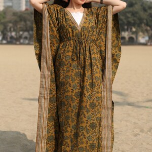 Puede incluir: Un vestido largo y fluido de kaft&aacute;n con estampado floral en tonos marrones y verdes. El vestido tiene un escote en V y una cintura con cord&oacute;n. La tela tiene un brillo sutil y una sensaci&oacute;n suave y c&oacute;moda.