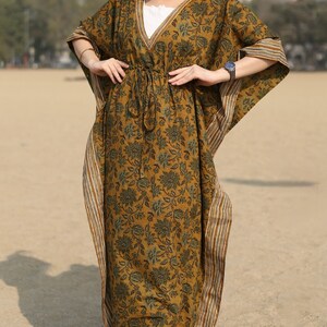 Puede incluir: Una kaftan larga y fluida con estampado floral en tonos marrones y verdes. La kaftan tiene un escote en V y una cintura con cord&oacute;n. La tela tiene un borde a rayas.