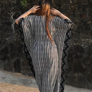 May include: A black and white striped kaftan with a black and white geometric pattern on the sleeves. The kaftan is flowing and loose-fitting.