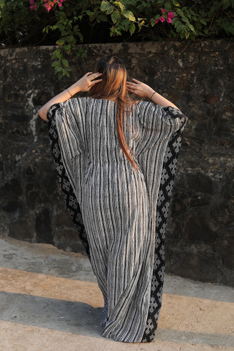 May include: A black and white striped kaftan with a black and white geometric pattern on the sleeves. The kaftan is flowing and loose-fitting.