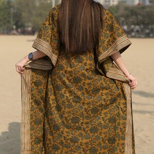 Puede incluir: Una larga kaft&aacute;n de color amarillo mostaza con estampado floral y ribete a rayas. La kaft&aacute;n tiene un corte holgado y es perfecta para un look casual y bohemio.