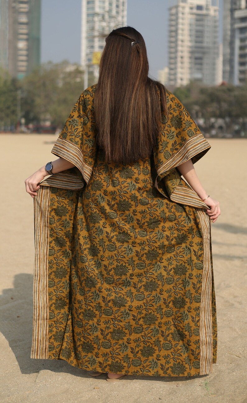 Puede incluir: Una larga kaft&aacute;n de color amarillo mostaza con estampado floral y ribete a rayas. La kaft&aacute;n tiene un corte holgado y es perfecta para un look casual y bohemio.