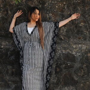 May include: A woman wearing a black and white striped kaftan with a black and white geometric pattern on the sleeves. The kaftan has a tie at the waist.