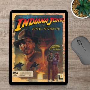 May include: A vintage video game box cover for Indiana Jones and the Fate of Atlantis. The cover features a colorful illustration of Indiana Jones, a woman, and a man in a jungle setting. The text "A Graphic Adventure by Hal Barwood" is printed on the cover.