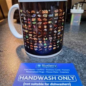 May include: A white ceramic mug with a black background and a design of various icons. The mug has a black handle and the text "HANDWASH ONLY (not suitable for dishwashers)" is printed on a blue and white card in front of the mug. The card also includes the text "Blueberry Design & Print" and "Etsy | Blueberryprintstore".