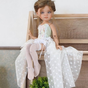May include: A handcrafted doll with a detailed face, wearing a floral bodice, a white skirt with polka dots, and white thigh-high stockings. The doll has brown hair and is posed sitting on a wooden shelf. The doll's outfit is accented with lace.