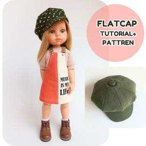 May include: A doll wearing a green polka-dot flat cap, a peach-colored top, and a white and orange overall dress with the text "MUSIC IS MY LIFE." The doll is also wearing brown boots. A second green flat cap is shown.