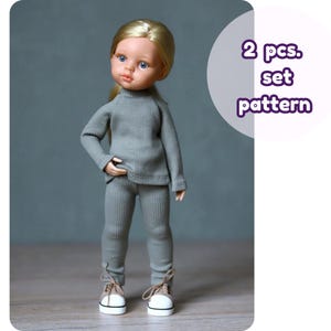 Puede incluir: Una muñeca vestida con un suéter de punto acanalado gris y pantalones a juego. La muñeca tiene cabello rubio y ojos azules, y lleva zapatillas blancas y beige. El texto a la derecha dice "2 pcs. set pattern".