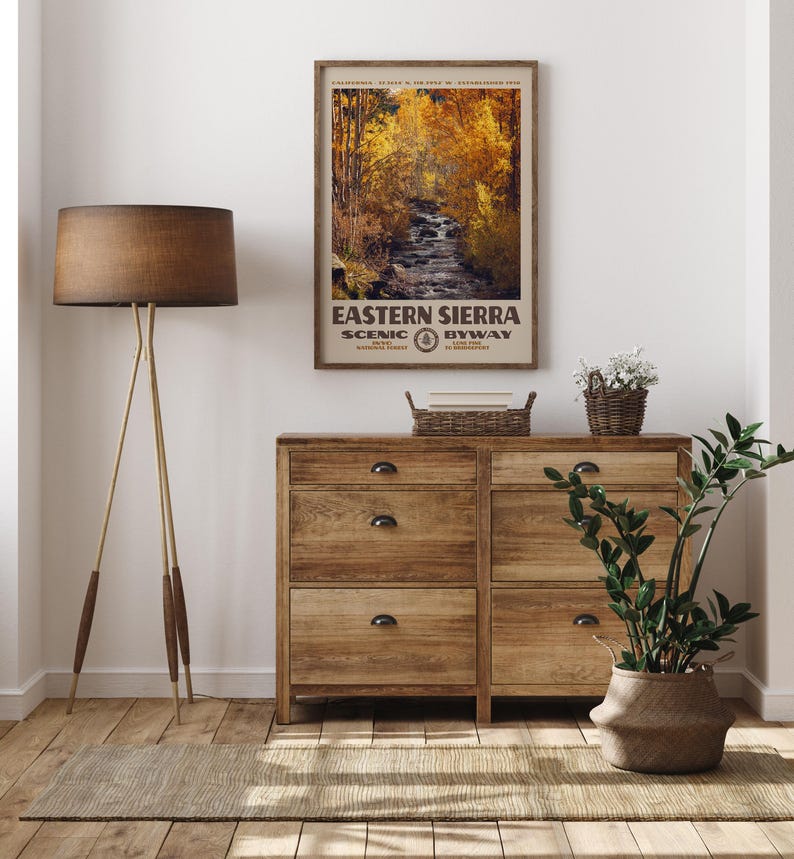 May include: A framed vertical wall art print titled Eastern Sierra Scenic Byway featuring a photograph of a flowing stream surrounded by golden autumn trees. The poster includes text detailing the location and establishment date of the route.