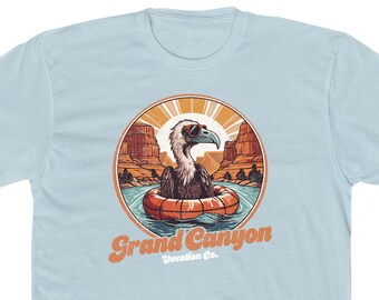 May include: A light blue t-shirt with a retro-style illustration of a cartoon vulture wearing sunglasses and floating on an orange inner tube in a river. The illustration is set against a backdrop of red rock cliffs and the text "Grand Canyon Vacation Co."