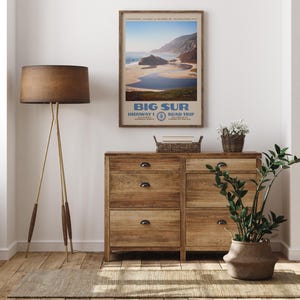 May include: A framed vertical wall art print featuring a scenic coastal landscape of Big Sur, California. The poster displays the text Big Sur, Highway 1, Road Trip, Los Padres National Forest, and California, with a blue ocean and sandy beach.