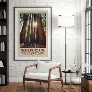 Puede incluir: Un p&oacute;ster enmarcado del Parque Nacional de las Secuoyas, que muestra altos &aacute;rboles de secuoya con la luz del sol filtr&aacute;ndose. El p&oacute;ster, con el nombre y el logotipo del parque, se exhibe en un sal&oacute;n con una silla y una l&aacute;mpara. El marco es negro.