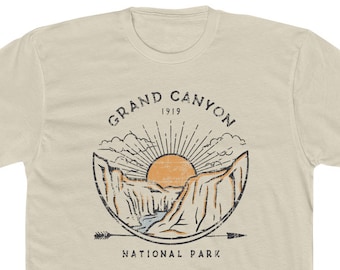 May include: A beige t-shirt with a vintage-style graphic of the Grand Canyon National Park. The graphic features a sun rising over the canyon with a river flowing through it. The text "Grand Canyon 1919 National Park" is printed in black.