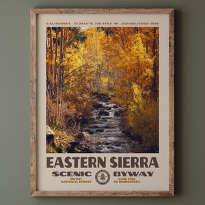 May include: A framed vertical poster featuring a photograph of a stream flowing through a forest with golden autumn leaves. The text reads CALIFORNIA 37.3614 N, 118.3952 W ESTABLISHED 1910, EASTERN SIERRA SCENIC BYWAY, INYO NATIONAL FOREST, LONE PINE TO BRIDGEPORT.
