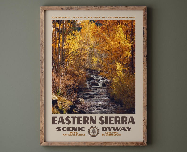 May include: A framed vertical poster featuring a photograph of a stream flowing through a forest with golden autumn leaves. The text reads CALIFORNIA 37.3614 N, 118.3952 W ESTABLISHED 1910, EASTERN SIERRA SCENIC BYWAY, INYO NATIONAL FOREST, LONE PINE TO BRIDGEPORT.