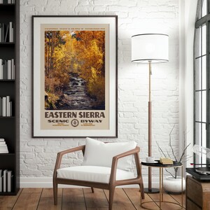 May include: A framed vertical poster featuring a photograph of a stream flowing through a forest with golden autumn foliage. The text reads EASTERN SIERRA SCENIC BYWAY, CALIFORNIA, 37.3634 N, 118.5954 W, ESTABLISHED 1910, INYO NATIONAL FOREST, LONE PINE TO BRIDGEPORT.