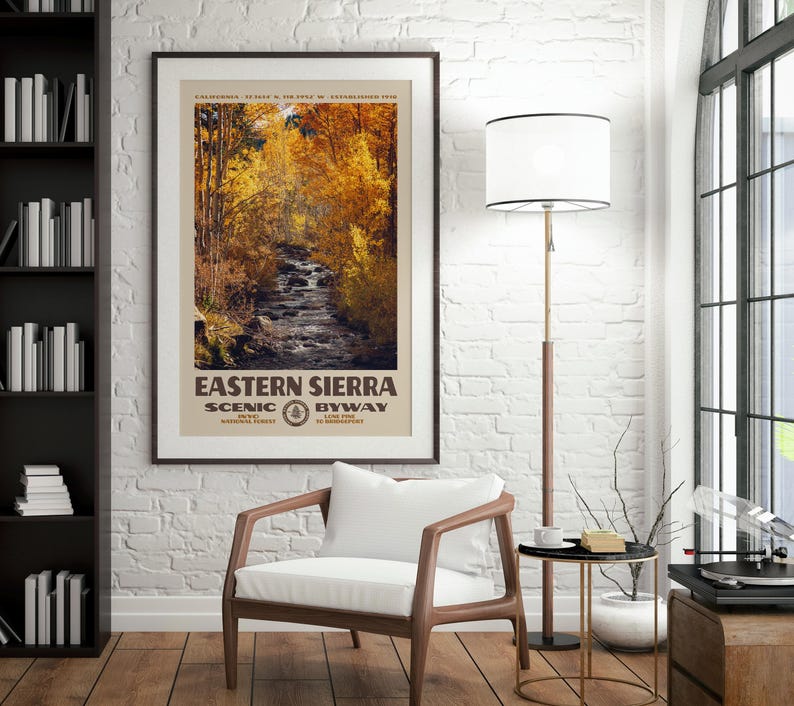 May include: A framed vertical poster featuring a photograph of a stream flowing through a forest with golden autumn foliage. The text reads EASTERN SIERRA SCENIC BYWAY, CALIFORNIA, 37.3634 N, 118.5954 W, ESTABLISHED 1910, INYO NATIONAL FOREST, LONE PINE TO BRIDGEPORT.