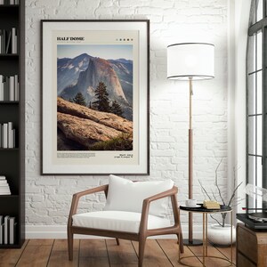May include: Framed art print featuring a photograph of Half Dome in Yosemite National Park. The image shows the mountain with a clear sky, trees, and rocky foreground. The print has a white border and is in a dark brown frame. Text at the top reads "HALF DOME".