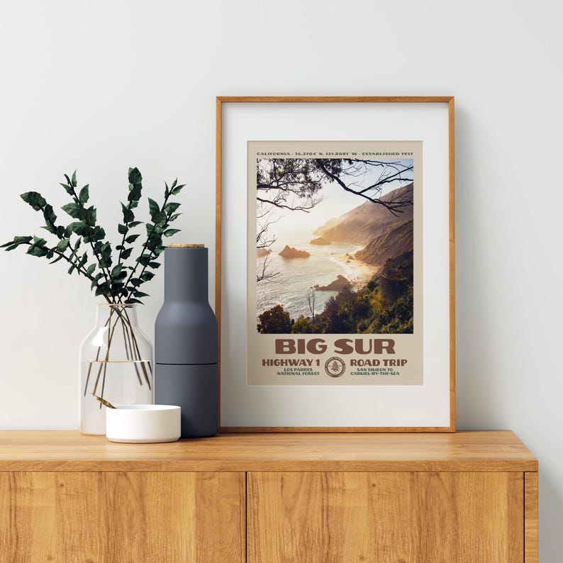 Pu&ograve; includere: Una stampa artistica da parete verticale incorniciata che raffigura un paesaggio costiero di Big Sur, California. L'immagine mostra scogliere rocciose, onde dell'oceano e alberi. Il testo recita BIG SUR, HIGHWAY 1 ROAD TRIP e dettagli locali.