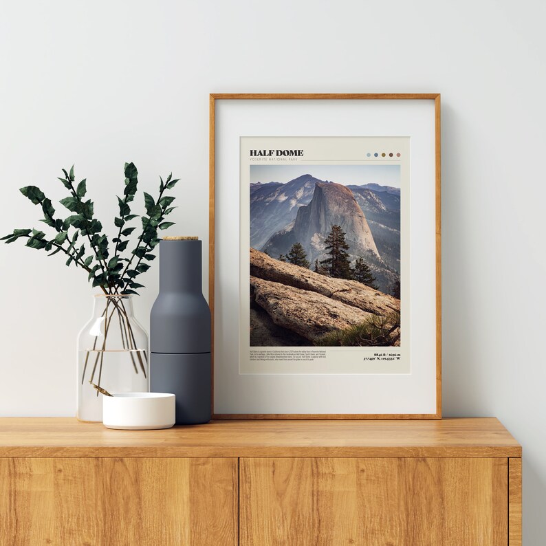 May include: A framed print featuring a photograph of Half Dome in Yosemite National Park. The image shows the mountain with a clear sky and text that reads "HALF DOME". The frame is a light brown color.
