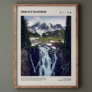 May include: A framed print featuring Mount Rainier National Park in Washington State. The image showcases a waterfall cascading down a rocky cliff, with a snow-capped mountain in the background. The print includes the park's name and date.