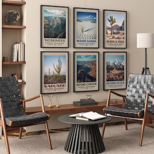May include: A collection of framed National Park posters, including Yosemite, White Sands, Joshua Tree, Saguaro, Grand Canyon, and Grand Teton. The posters are displayed on a beige wall above a wooden console. Two black leather chairs and a round black table are in the foreground.