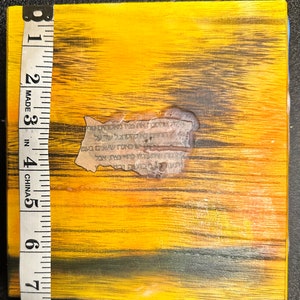 May include: A yellow wooden box with black wood grain and a torn piece of paper with Hebrew text on it. The box is 7 inches tall.