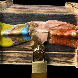 May include: A wooden box with a colorful resin inlay and a brass padlock. The box has metal hinges and a distressed wood finish.