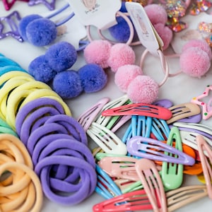 May include: A collection of colourful hair accessories, including pastel-coloured hair ties, rainbow-coloured barrettes, and star-shaped clips.