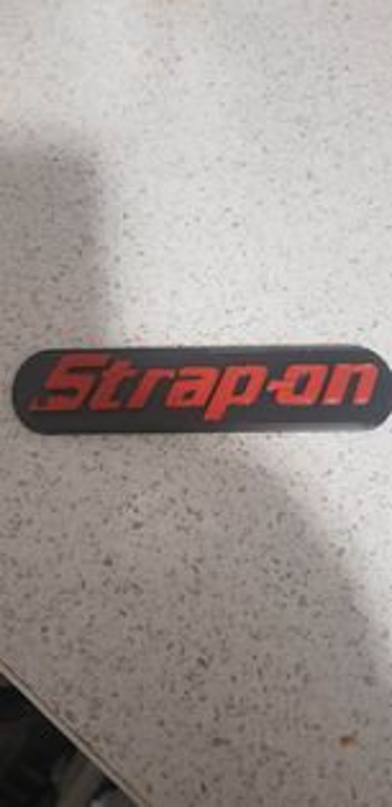 May include: A black and red plastic emblem with the text "Snap-on" in red letters.