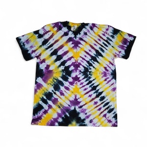 May include: A short-sleeve t-shirt featuring a tie-dye pattern with diagonal stripes in black, yellow, purple, and white. The shirt has a crew neckline and solid black trim on the sleeve cuffs, creating a geometric diamond effect across the front.
