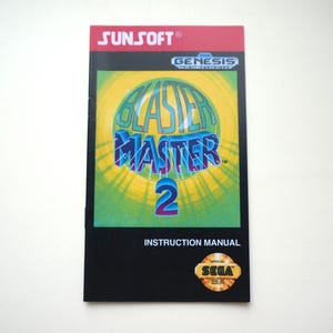 May include: A rectangular instruction manual for the Sega Genesis video game Blaster Master 2. The cover features the Sunsoft logo, the Sega Genesis logo, and a central graphic with the title text in blue and purple against a yellow sunburst.