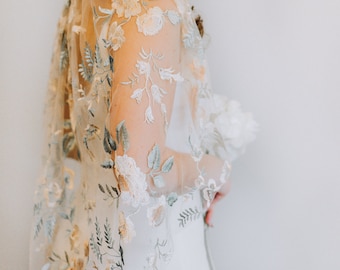 May include: A sheer, ivory-colored bridal veil with delicate floral embroidery in shades of green, beige, and white.