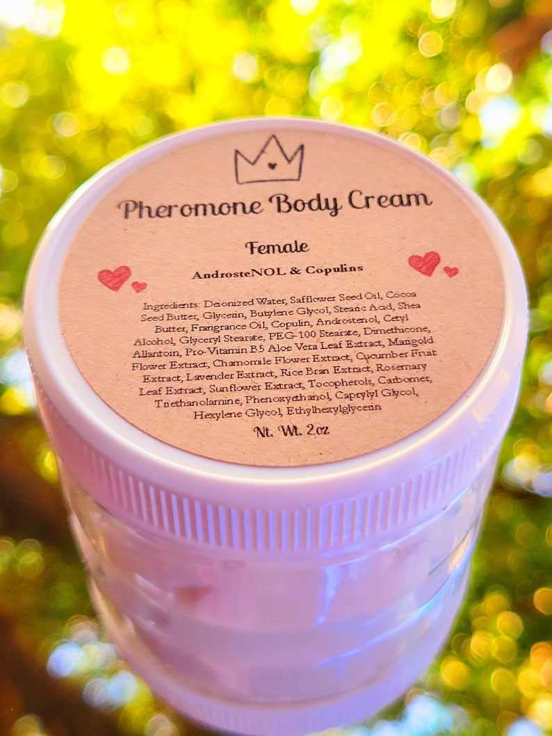 May include: A pink jar with a white lid and a label that reads "Pheromone Body Cream Female AndrosteNOL & Copulins". The label lists the ingredients of the cream, which include deionized water, safflower seed oil, cocoa seed butter, glycerin, butylene glycol, stearic acid, shea butter, fragrance oil, copulin, androstenol, cetyl alcohol, glyceryl stearate, PEG-100 stearate, dimethicone, allantoin, pro-vitamin B5, aloe vera leaf extract, mangold flower extract, chamomile flower extract, cucumber fruit extract, lavender extract, rice bran extract, rosemary leaf extract, sunflower extract, tocopherols, carbomer, triethanolamine, phenoxyethanol, caprylyl glycol, hexylene glycol, ethylhexylglycerin. The label also states "Nt. Wt. 2oz".