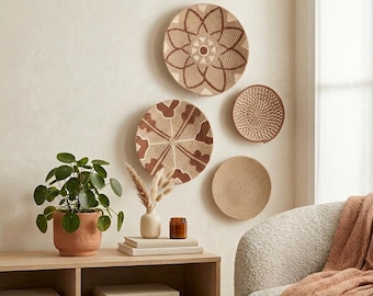 May include: A collection of woven wall baskets in various sizes and patterns, displayed on a neutral-colored wall. The baskets feature natural tones of beige and brown. A potted plant and decorative items sit on a wooden shelf below.