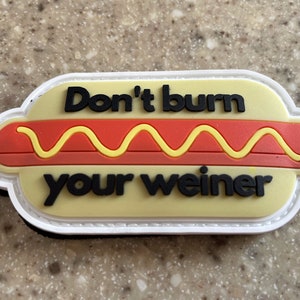 May include: A white, yellow, and red patch with a hot dog design. The text on the patch reads "Don't burn your weiner."