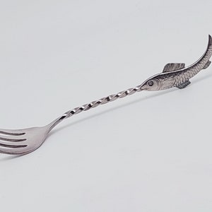 May include: A silver fish-shaped cocktail fork with a twisted handle and a three-pronged fork.