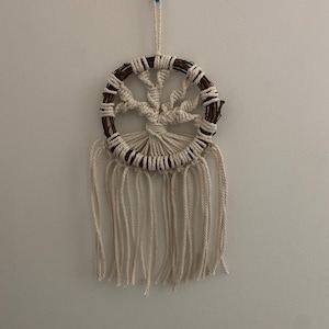 May include: A white macrame tree of life wall hanging with a brown twig circle frame and white fringe.