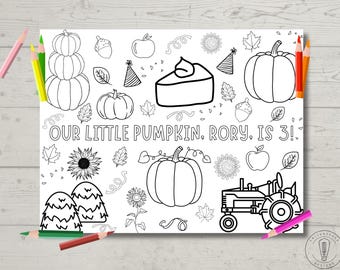 Puede incluir: Una página para colorear en blanco y negro con un tema otoñal. La página presenta calabazas, hojas, un pastel, un tractor y el texto "Nuestra pequeña calabaza, Rory, ¡tiene 3 años!"