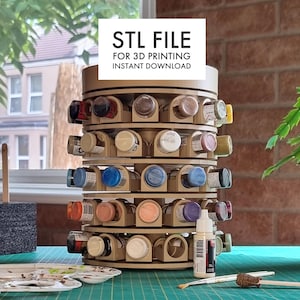 Puede incluir: Un organizador de pintura giratorio impreso en 3D con múltiples niveles para guardar pequeños frascos de pintura. El organizador está hecho de plástico beige y tiene una base circular. El texto "STL FILE FOR 3D PRINTING INSTANT DOWNLOAD" está impreso en la parte superior del organizador.
