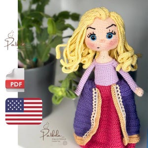 Könnte beinhalten: Eine handgefertigte Häkelpuppe mit blonden Haaren, blauen Augen und einem lila-rosa Kleid. Die Puppe hat ein detailliertes Gesicht und trägt ein lila Oberteil. Der Artikel ist handgefertigt.