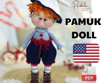 Puede incluir: Patrón de muñeca de crochet para una linda muñeca de niño que lleva un atuendo azul y rojo, un sombrero blanco y gafas. El patrón está disponible para descargar en PDF. La imagen también incluye el texto "Pamuk Doll" y una bandera de Estados Unidos.
