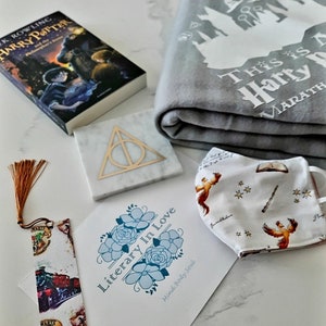 May include: A Harry Potter themed gift basket featuring a book, a blanket, a face mask, a bookmark, a coaster, and a card that reads "Literary In Love".