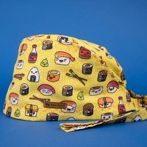 May include: Yellow surgical scrub hat with a fun sushi print featuring cartoon sushi rolls, soy sauce bottles, and rice balls. The hat has a black adjustable tie.