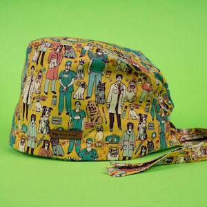 May include: A yellow scrub cap with a repeating pattern of veterinarians, dogs, and medical supplies. The cap has a brown tag with text and a matching tie. The background is a solid green.