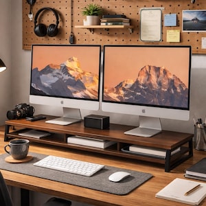 May include: A home office setup featuring two computer monitors displaying a mountain landscape. A wooden monitor stand holds a keyboard, mouse, and other office supplies. A black desk lamp, headphones, and a small potted plant are also visible.
