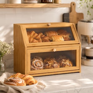 Peut inclure: Une boîte à pain en bambou à deux niveaux avec des fenêtres en verre transparent sur les panneaux avant. Le compartiment supérieur contient plusieurs croissants dorés, tandis que le compartiment inférieur contient diverses pâtisseries.